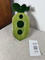 Full view of vintage green ceramic serving platter shaped as a pea pod with three raised peas and a ceramic peg for hanging.