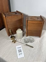 Photo showing two wooden canisters, stoneware bottle, two glass salts, brass coffee measure, and brass candle snuffer all arranged on a surface.