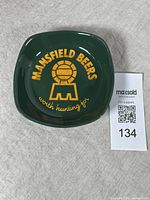 Top view photo of green ceramic dish with Mansfield Beers logo and slogan in yellow lettering on surface. Shows full design and color.