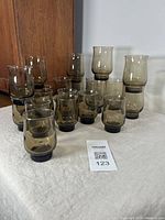 Photo showing the full set of 21 smoked vintage glasses arranged on cloth surface with wooden panel backdrop.