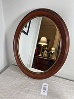 Full view of the oval mirror with walnut wooden frame leaning against a white wall, reflecting interior room elements.