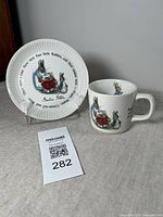 Set of a Peter Rabbit illustrated plate and cup displayed on tabletop.