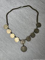 Full view of the WW2 era coin necklace with 9 coins attached to a metal chain on a neutral fabric background