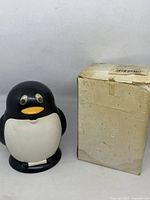 Front view of penguin ashtray beside worn box