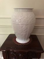 Front view of the glossy white Wedgwood fluted vase showing the full height, placing the vase on a dark wood table with a decorative underlay.