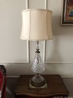 Full view of the antique crystal glass table lamp showing the fabric shade and the crystal glass body on the wooden surface.