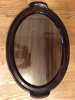 Top down view of oval tray showing dark mahogany wood frame, inset glass top, and carved wooden handles.