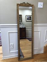 Full view of the tall antique mirror with solid wood carved gold frame leaning against a wall.