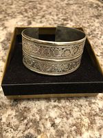 Silver cuff bracelet displayed on black velvet with gold tray base, showing detailed front design and structure.