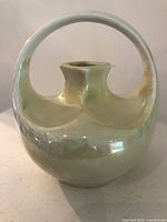 Front view of the miniature yellow lustre porcelain vase with loop handle showing its oval bulbous shape and square neck.