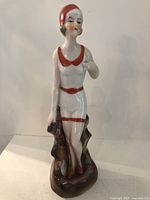 Front view of the porcelain bathing beauty figurine with white and red swimsuit and bathing cap, standing on a brown base