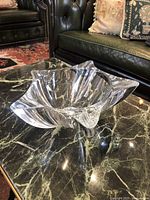 Crystal Bohemia Yoko Large Bowl photographed on a marble table with leather furniture in the background. The bowl is clear, sculptural with dynamic flame-like design.
