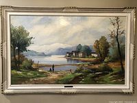 Full view of large framed oil painting on canvas showing lakeside landscape with people and houses.