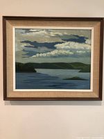 Framed painting on wall showing full composition of lake, hills and clouds
