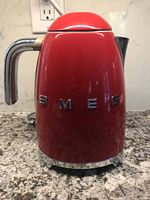 Frontal view of the red Smeg kettle on a kitchen counter with SMEG lettering visible.