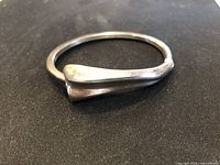 Side angle of the sterling silver cuff bracelet showing the tapered overlapping ends and polished surface.