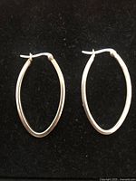 Pair of silver oval hoop earrings displayed on black background, showing full front view of both earrings.