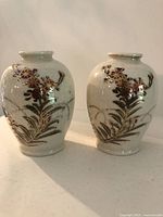 Front view of two antique miniature vases with hand-painted floral designs in gold and dark red on a crackle-glazed white background.