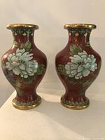 Front view of two vintage Chinese cloisonne vases with white flower motif, brass rims, and reddish cloisonne background.
