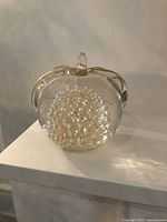 Front view of clear glass apple paperweight showing controlled bubble pattern inside and smooth curved glass exterior with stem and leaf shape.