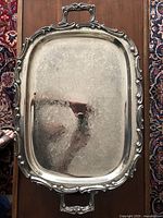 Top down photo of large silver plated butler serving tray showing ornate floral etching and decorative footed handles along edges.