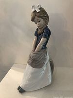 Front and side views of the NAO by Lladró girl figurine showing the detailed facial features, clothing colors, and glossy finish.