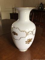 Front and side view of white porcelain vase showing gold floral decorations and gold scrollwork