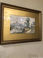 Framed watercolor painting showing a bridge over a river with trees and figures on a path, set in an ornate gold-colored carved frame.