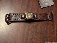 Full view of Fossil men's watch laid flat showing brown leather strap with embossed floral design and two snap buttons