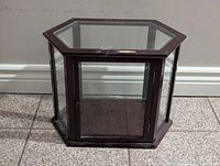 Front view of hexagonal glass display case showing dark brown wood frame, glass panels, and front door with latch.