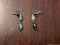 White and black baroque pearl dangle earrings on a wood surface, showing pair and details of pearls.