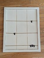 Front view of white framed wall card display showing three horizontal twine strings with black clips attached for hanging cards.