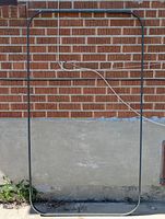 Metal frame for outdoor picnic table standing vertically against a brick wall, showing rectangular shape with rounded corners, and a cord draped inside.