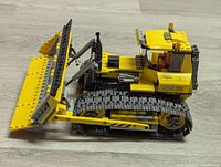 Side view showing yellow bulldozer with black tracks, adjustable front blade, and minifigure in cab