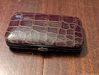 Closed manicure set case showing the faux crocodile texture and snap closure on a wooden surface.