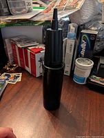 Black manual air pump on a cluttered desk with art supplies and other items in background.
