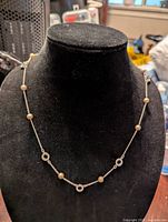 Necklace displayed on black jewelry stand showing silver tone chain with pearls and circular charms.