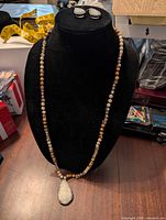 Photo of jewelry set showing necklace with small round beads in tan, cream, and light green imitation jade colors, featuring a teardrop-shaped pendant with rhinestone druzy drop. Matching oval-shaped rhinestone druzy earrings shown.