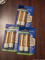 Photo showing three unopened packs of Nivea Vanilla Buttercream Lip Balm, each pack contains two lip balm sticks in golden and white tubes.