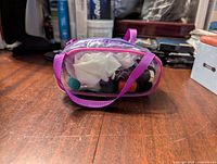 Clear plastic pouch with purple trim showing sewing threads, needles, and other sewing accessories inside.