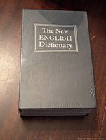 Image of dictionary safe front cover showing title 'The New English Dictionary' in gold embossed text on a grey textured cover.
