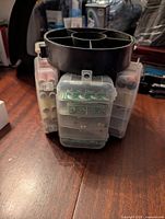 Front view of black rotating sewing organizer showing attached clear compartments with various buttons and sewing items inside