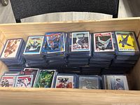 Over 1000 sleeved and top loaded sports cards arranged in stacks inside a wooden drawer. Visible cards include various sports like baseball and football.