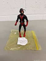 Front view of the Ant-Man action figure standing on a yellow plastic bag with a handwritten note.