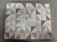 Box packaging with geometric cream, pink, and gray triangle pattern and Coffee Mania branding