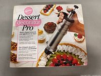 Front box image of Wilton Dessert Decorator Pro showing the piping syringe in use on plated desserts and appetizers.