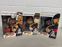 Front view of the three Mighty Muggs figures in their original boxes, showing Indiana Jones, Mola Ram, and Cairo Swordsman characters with packaging details.