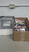 Two gray Hockey Collector binders, a small white short box and a large cardboard box of loose hockey cards on the floor