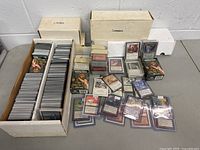 Two white cardboard boxes labeled "Lands" and "Commons" filled with Magic cards, with loose cards and sleeves displayed in front.