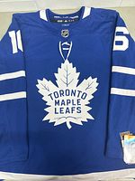 Front view of blue Toronto Maple Leafs hockey jersey with white leaf logo and Mitch Marner number 16 on sleeves.